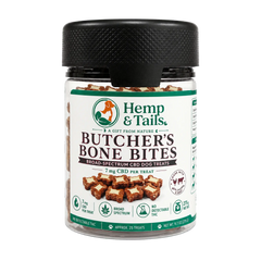 A jar of Hemp & Tails Butcher's Bone Bites dog treats, featuring a black textured lid and a white label with green and brown accents, set against a plain white background.